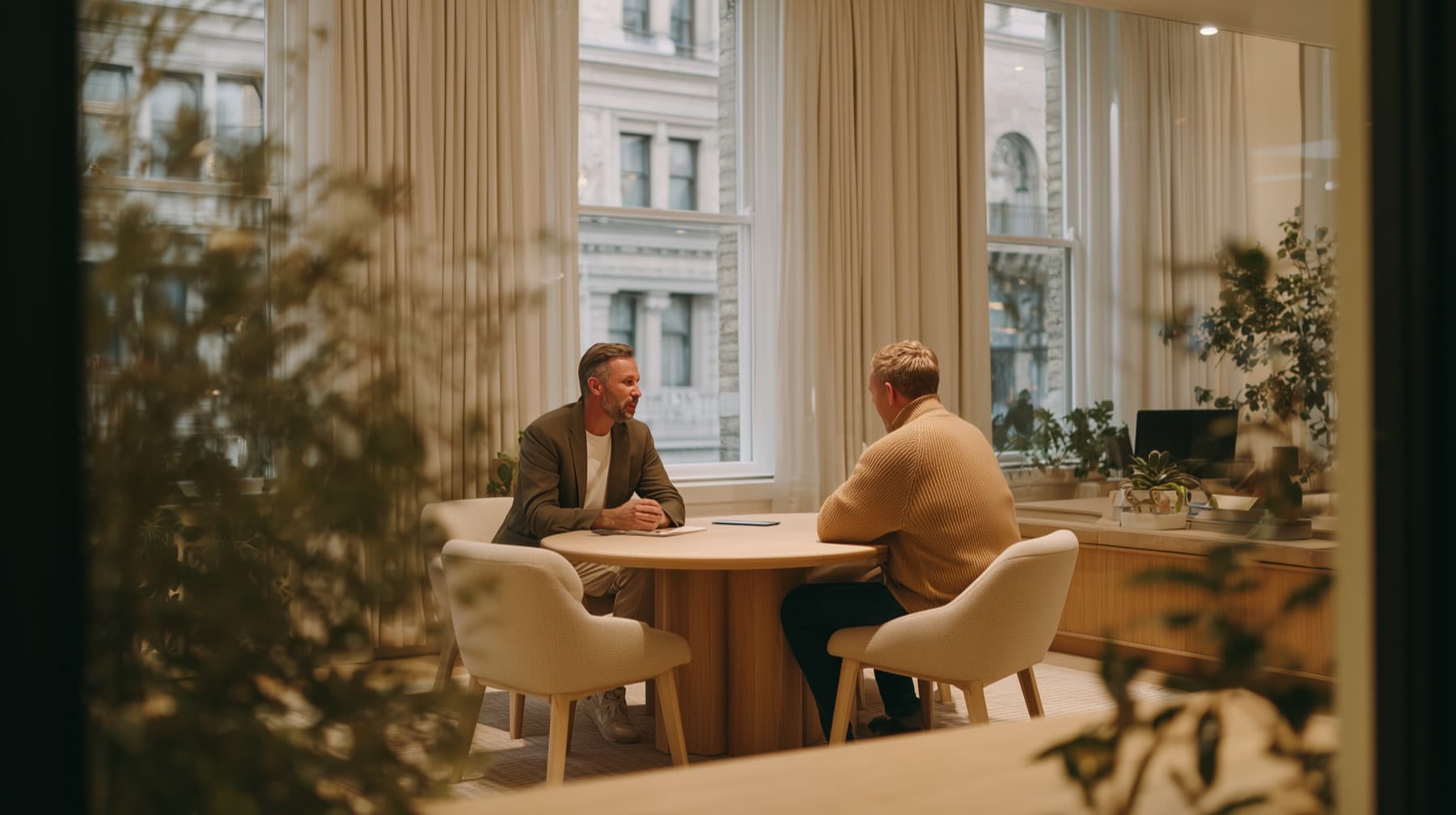 Adviser and client meeting across a round oak table in a light-filled office
